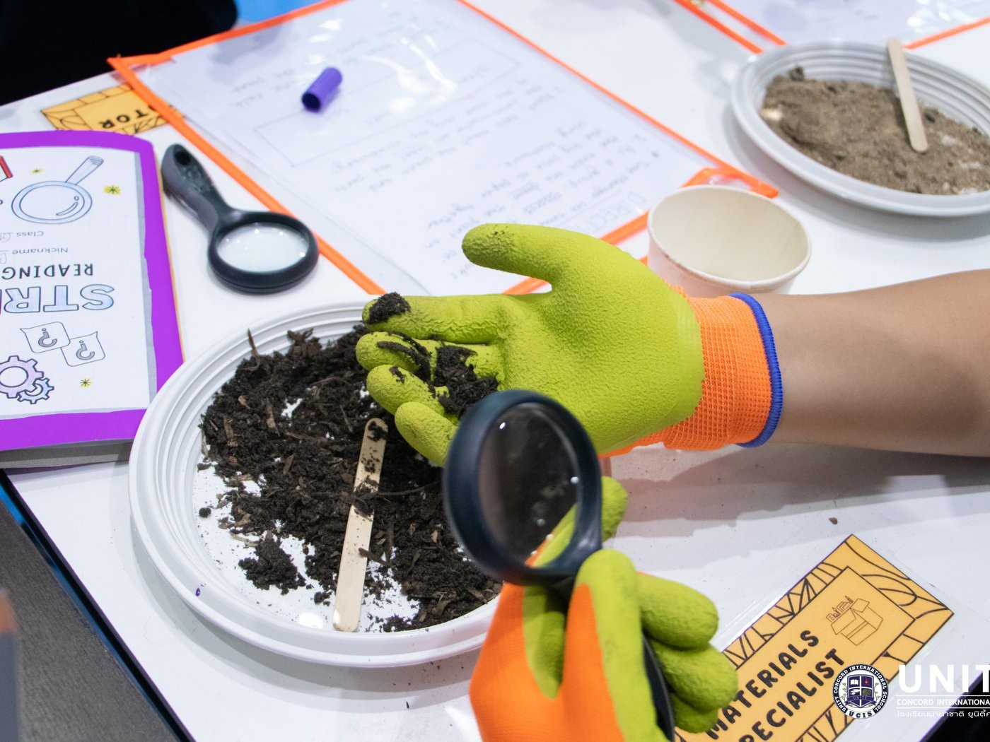 Student examining finished compost with a magnifying glass and recording observations in a reading journal