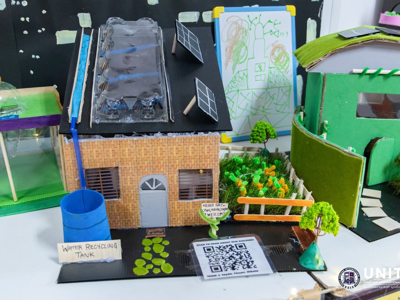 Finished cardboard green building model with a water recycling tank, solar panels, and garden