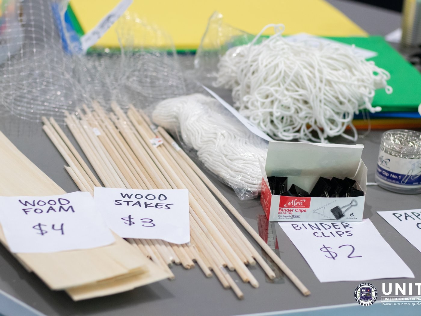 Priced makerspace materials laid out for students to shop for their ocean-cleanup device, including wood stakes and binder clips