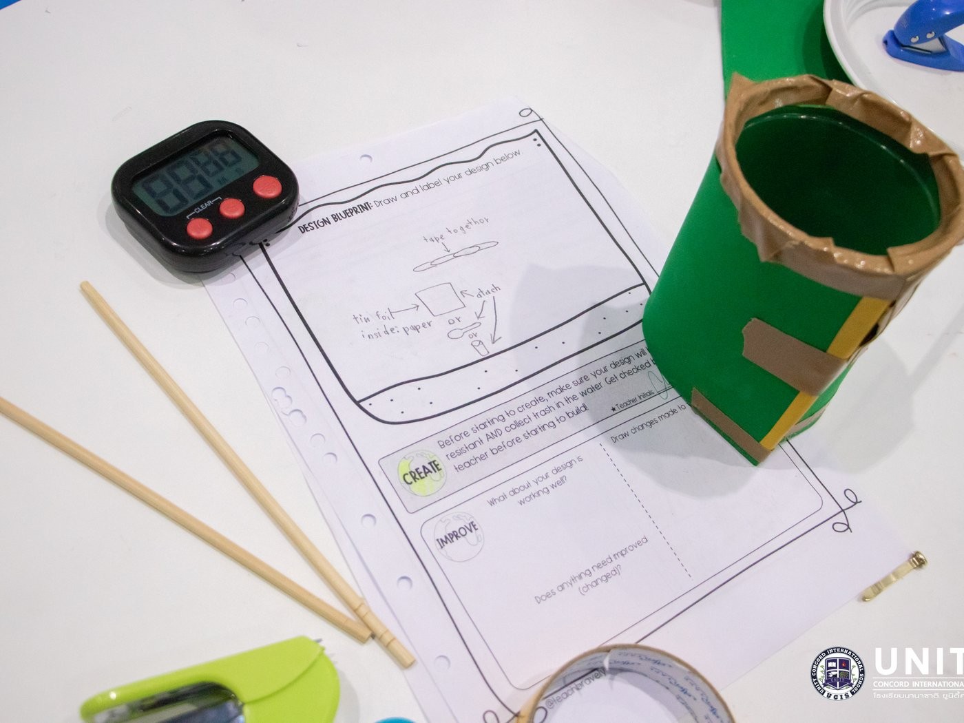 A design blueprint worksheet next to a student's prototype ocean-cleanup device