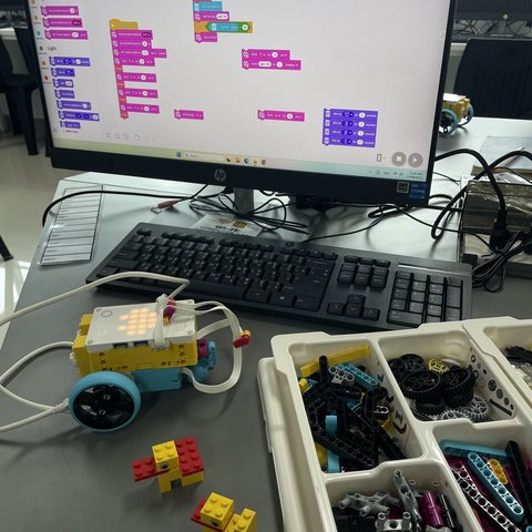 Students at a desk with a LEGO SPIKE robot and Scratch code on screen