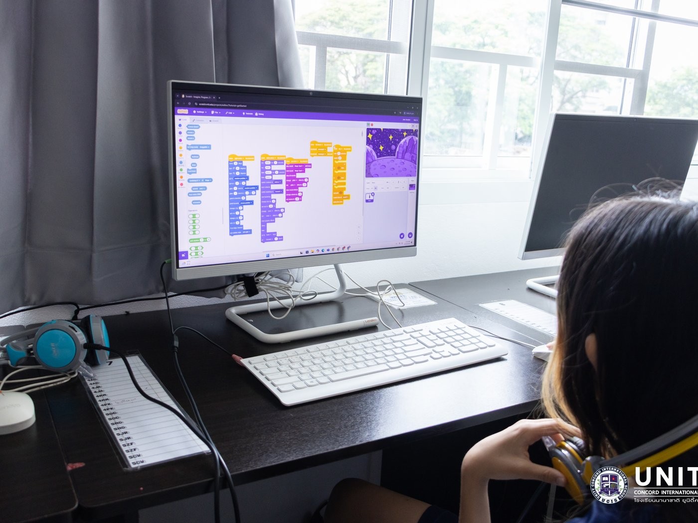 Student writing Scratch code blocks to animate a space-themed project