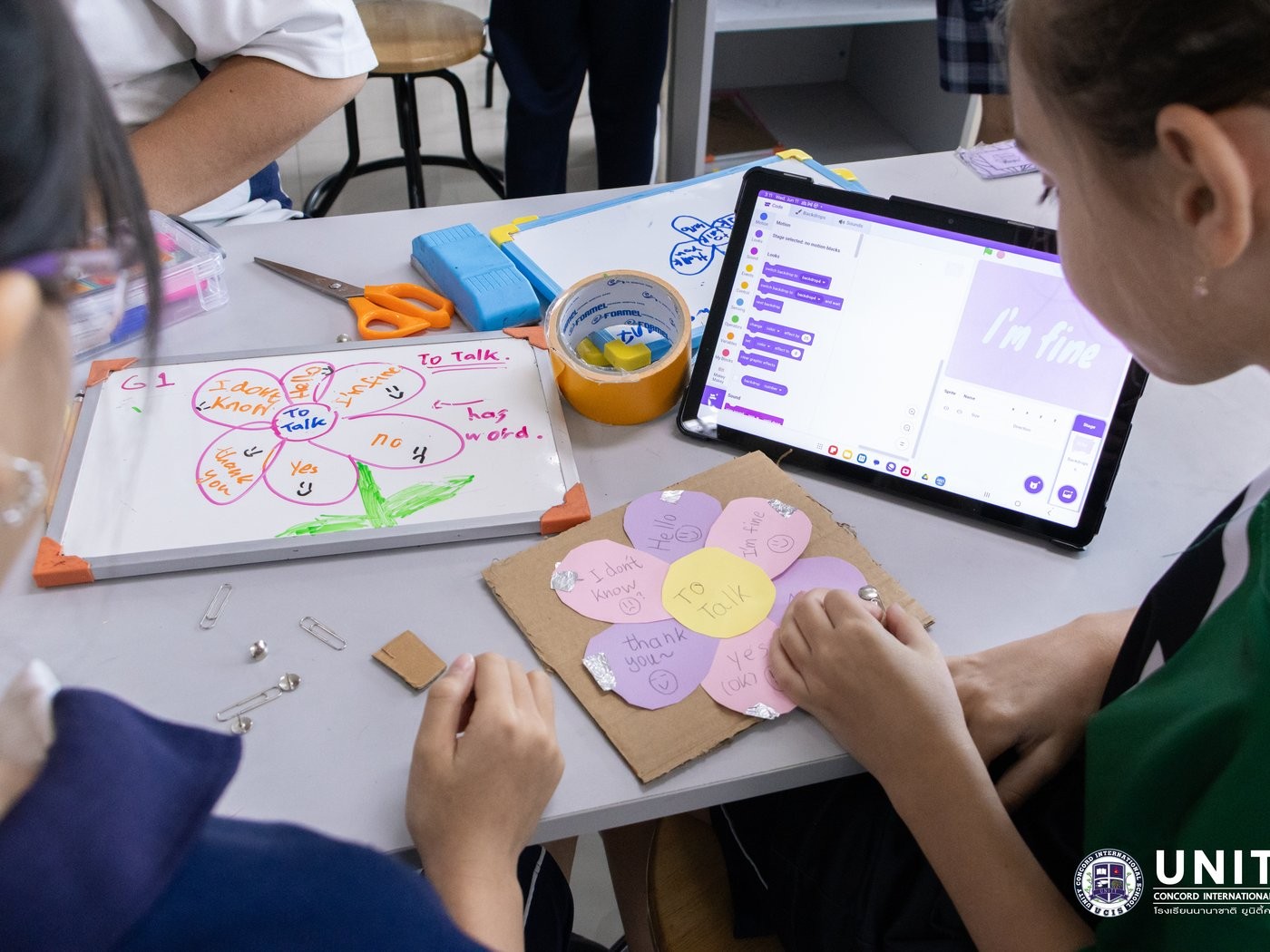 Students building a cardboard flower AAC device with common phrases, wired to a Makey Makey and Scratch project reading 'I'm fine'